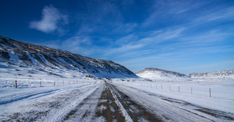 A snowy road with dark hills and blue sky in the distance.