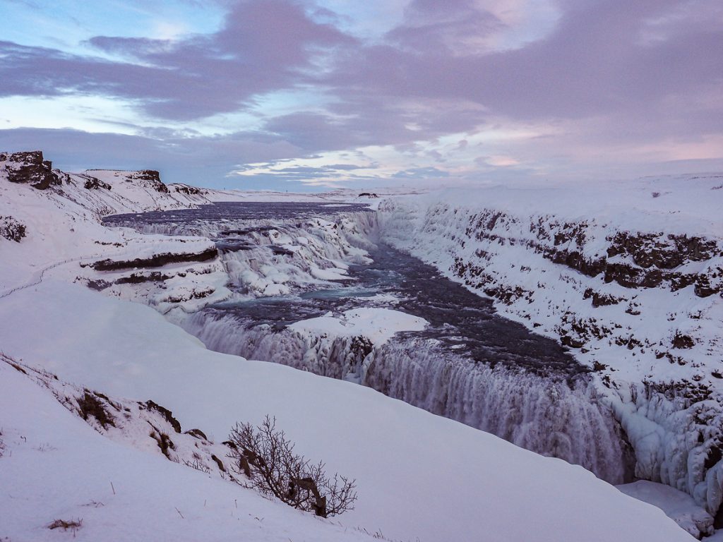 A series of waterfalls surrounded by a snowy landscape and cloudy sky.