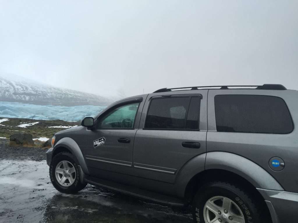 A dark gray 4x4 car parked next to rocks and ice on a very overcast day.