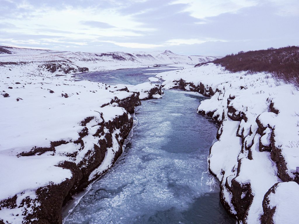 A frozen river with snow covered black rocks on either side.