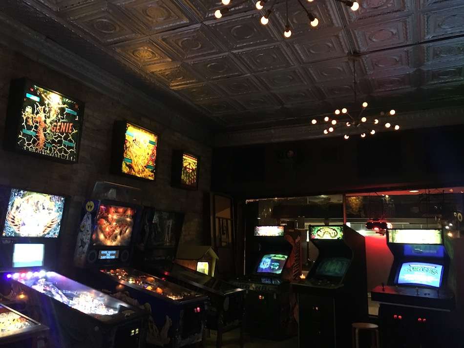 A dark room with lit up pinball machines and arcade games.