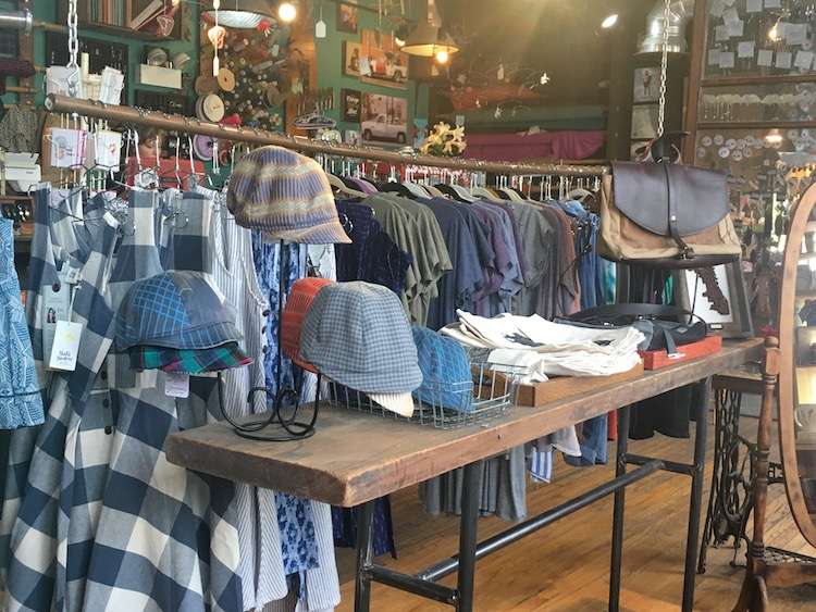 A table of hats in front of racks of clothing inside a shop.