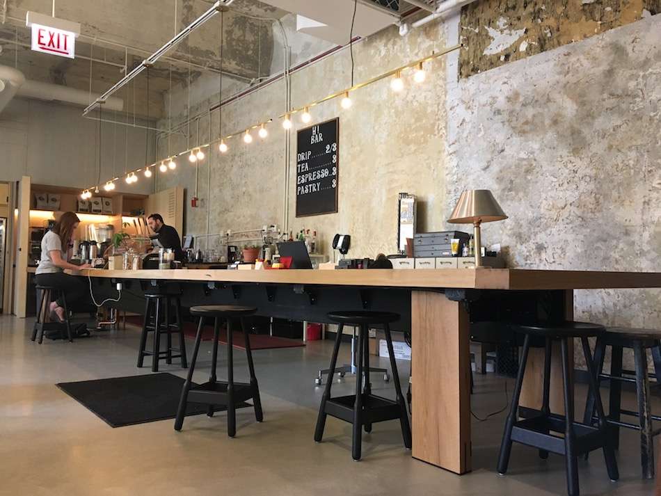 An open coffee/co-working space with concrete walls and a long wooden table.