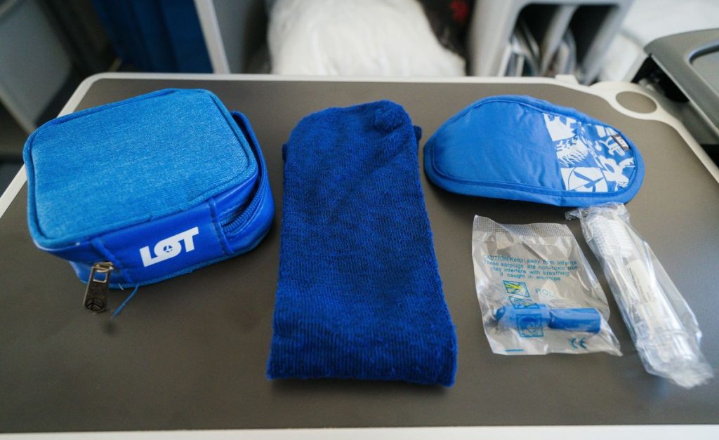 An airplane tray table with blue items including ear plugs, eye mask and tooth brush, wrapped in plastic.