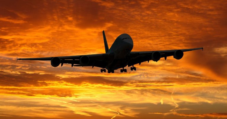 An airplane in flight silhouetted against clouds in intense yellows and orange.