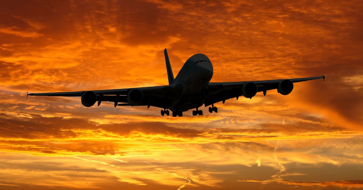An airplane in flight silhouetted against clouds in intense yellows and orange.