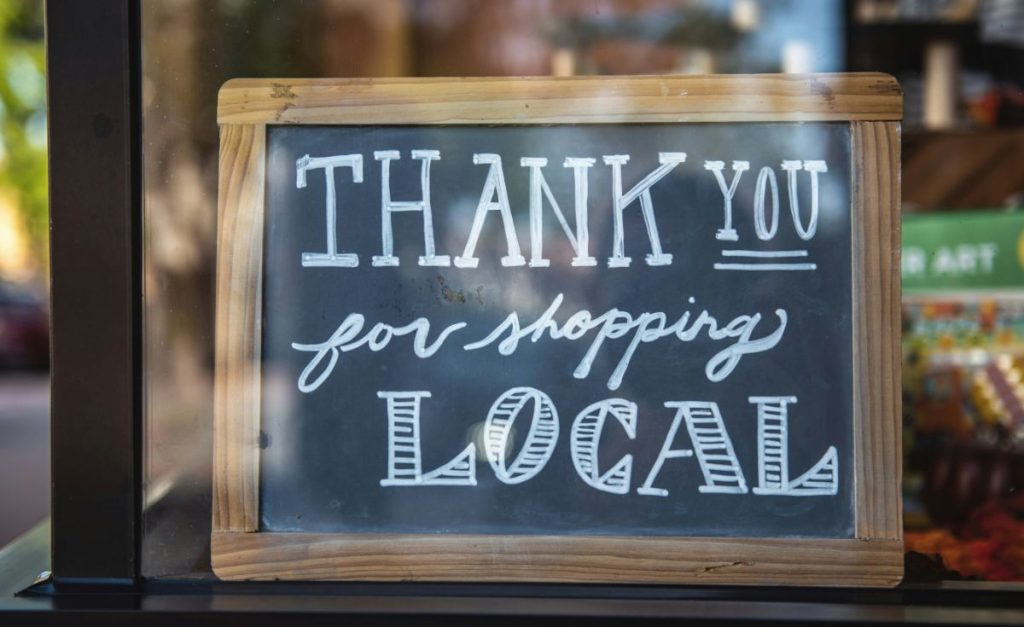 A photo of a chalkboard sign in a window that says "thank you for shopping local."
