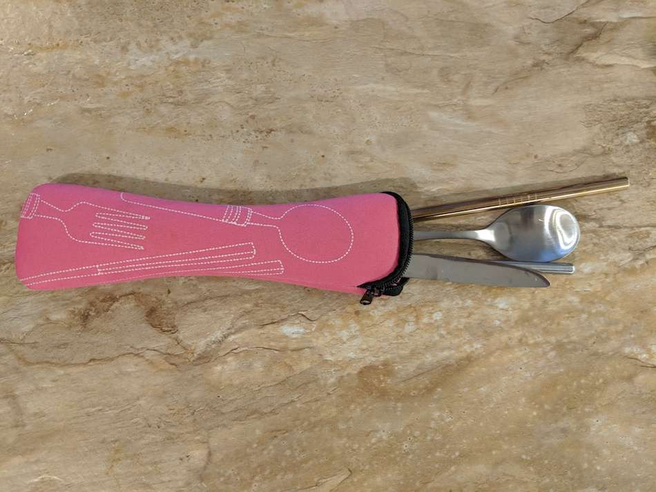 A pink case holding metal food utensils on a wooden surface.