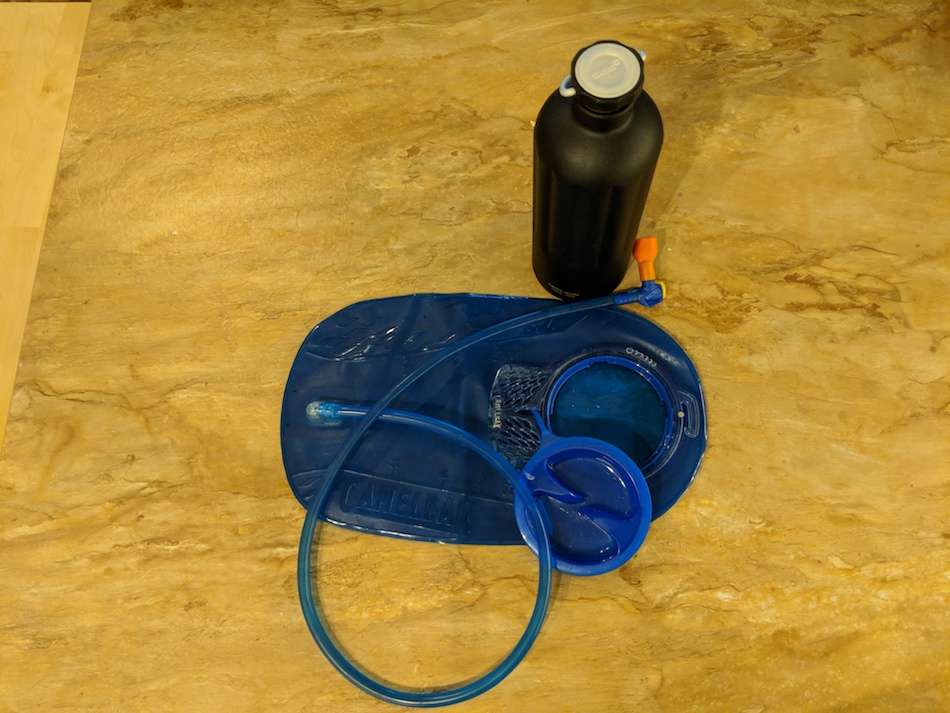 A water bladder for a backpack and a reusable water bottle sitting on a wooden surface.