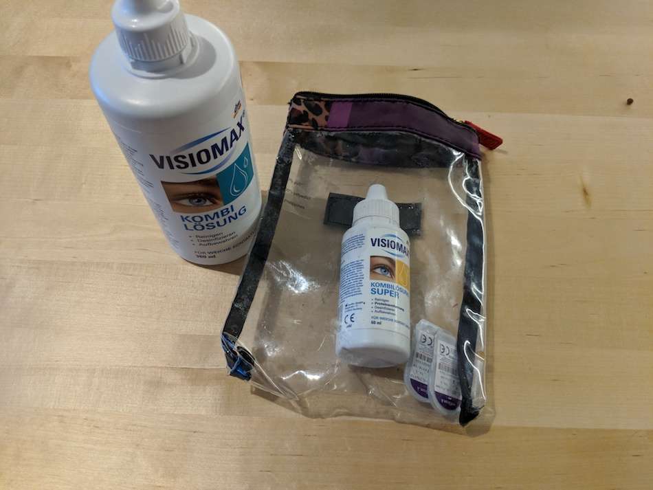A big bottle of contact lens fluid next to a smaller bottle inside a clear plastic case.