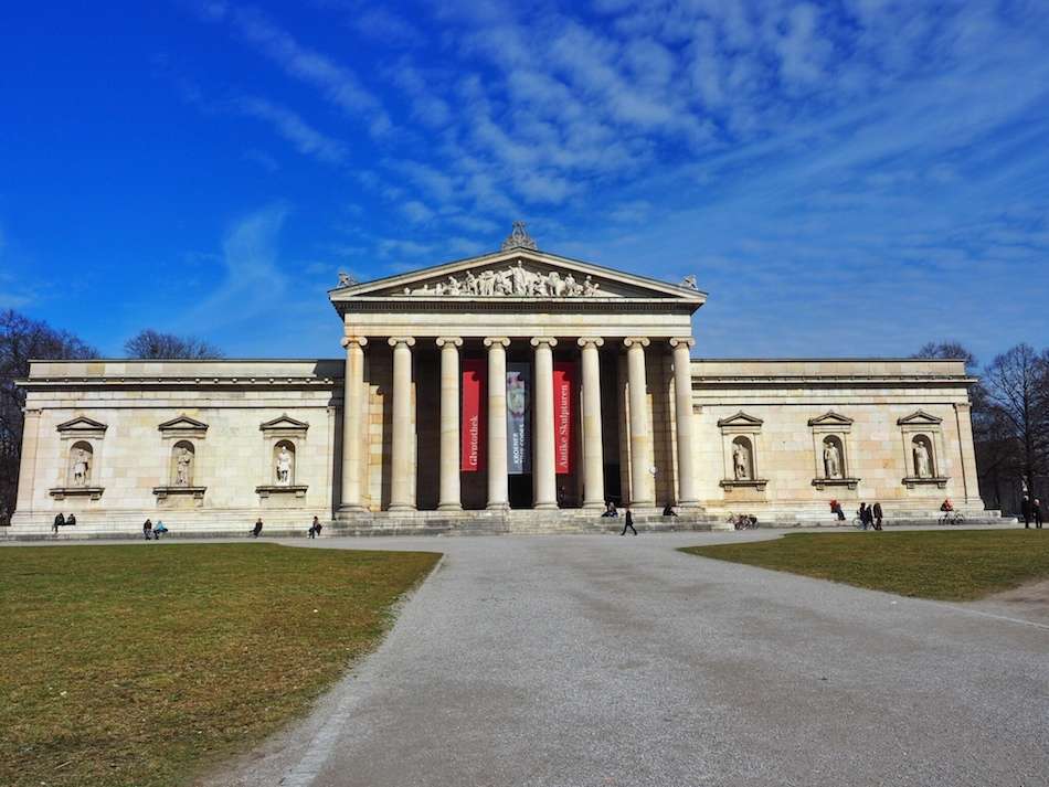 A museum in Munich at Königsplatz with tall columns in the middle and statues in the walls on either side of the columned portico.