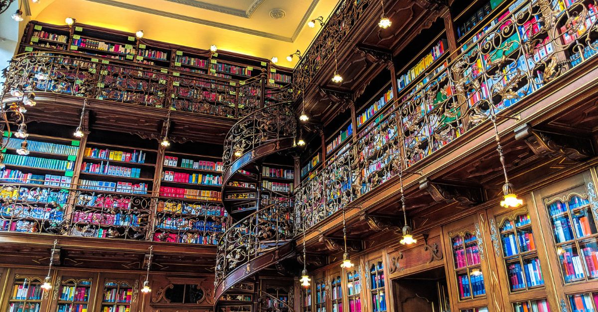A room covered in bookshelves with platforms and a spiral staircase with ornate scrolled railings and fancy lights.