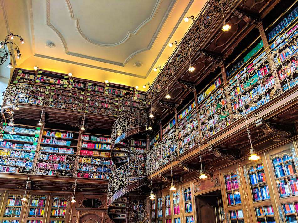 A room covered in bookshelves with platforms and a spiral staircase with ornate scrolled railings and fancy lights.