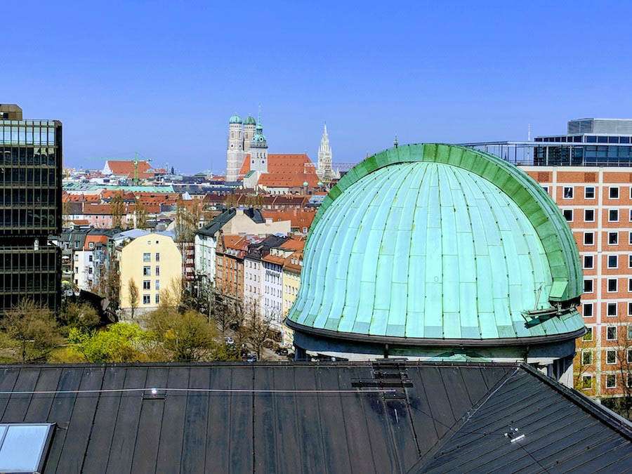 An aqua colored dome on a roof with more roofs in the background and blue sky.