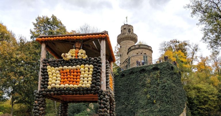 A person and fort make out of pumpkins, standing in front of a castle tower covered in ivy.