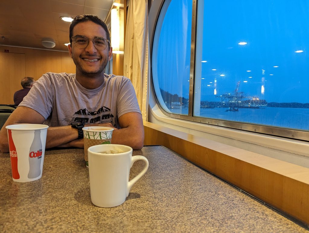Ganesh smiling while sitting next to a window in the Coastal Cafe with three different cups on the table in front of him.