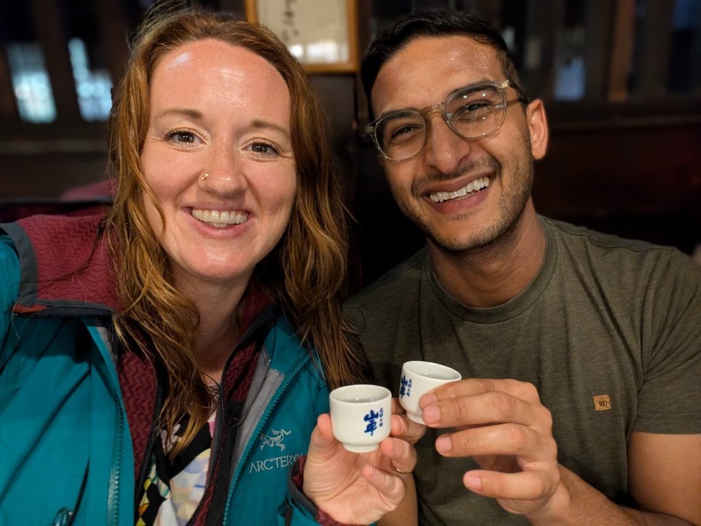 Sooz and Ganesh clinking their sake cups together while smiling at the camera.