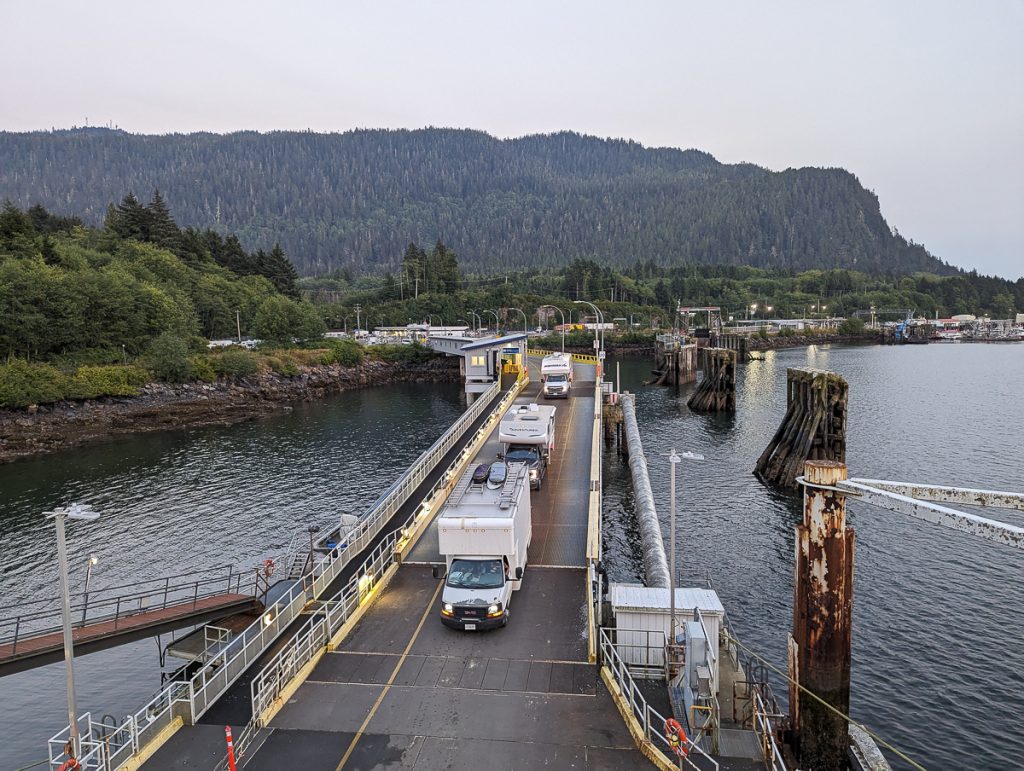 A view of campervans boarding a ferry, as seen from above on board the ferry looking towards land.