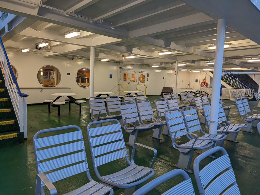 Blue chairs and picnic tables bolted to the outside deck of a BC Ferry, at night.