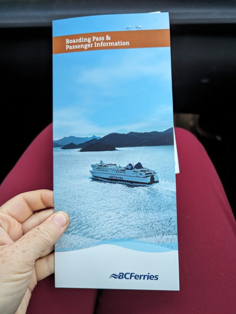 A close-up shot of a hand holding a brochure with a photo of a ferry and text saying "Boarding pass & Passenger Information BC Ferries."