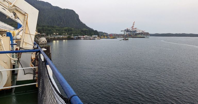 A view of water and constructions from the deck of a ferry on an overcast day.