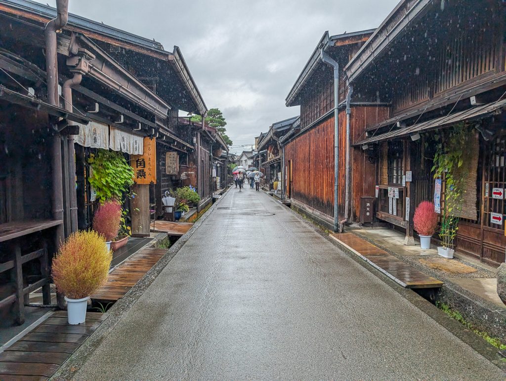 A cute street in the Old Town of Takayama with people walking holding umbrellas in the distance.