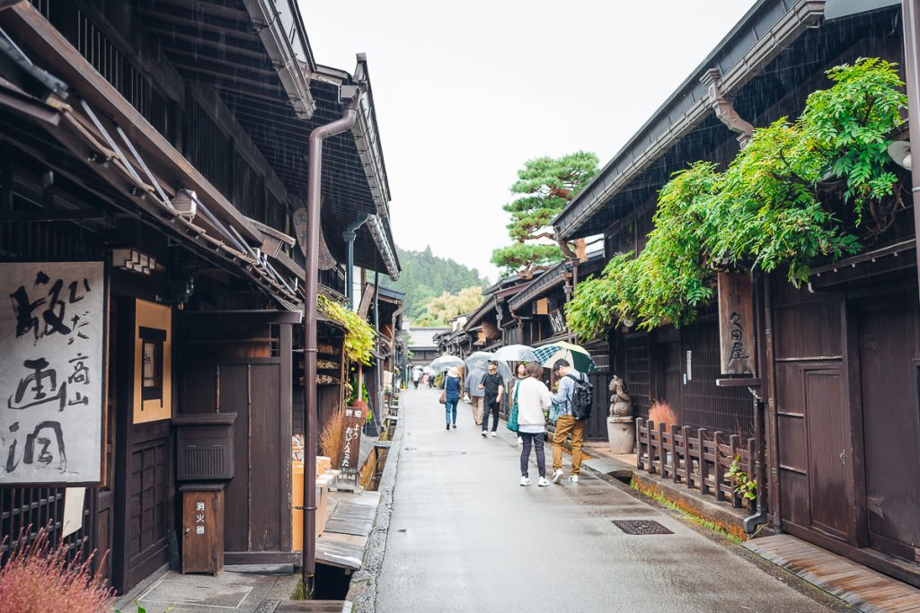 A street in Takayama, Japan with wooden buildings and signs with kanji script plus people with umbrellas.