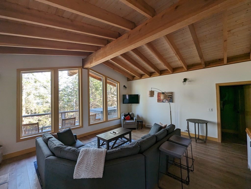 A spacious lounge room with wooden beams and a big couch looking towards big windows.