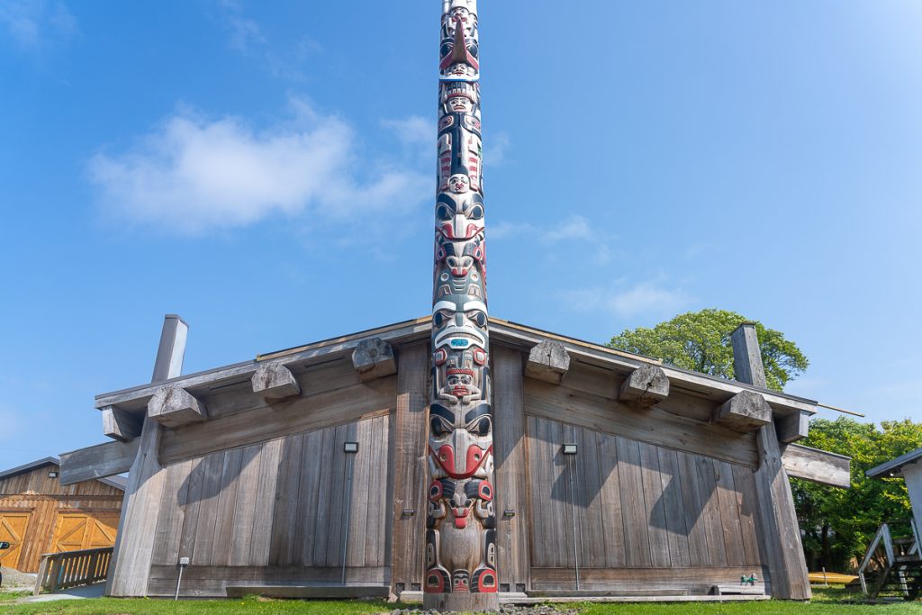 A wooden building with a wooden totem pole in front with a clear blue sky behind.