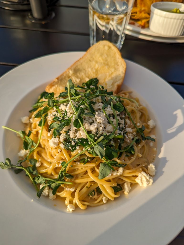 A close up plate of pasta with crumbled cheese and greens on top.
