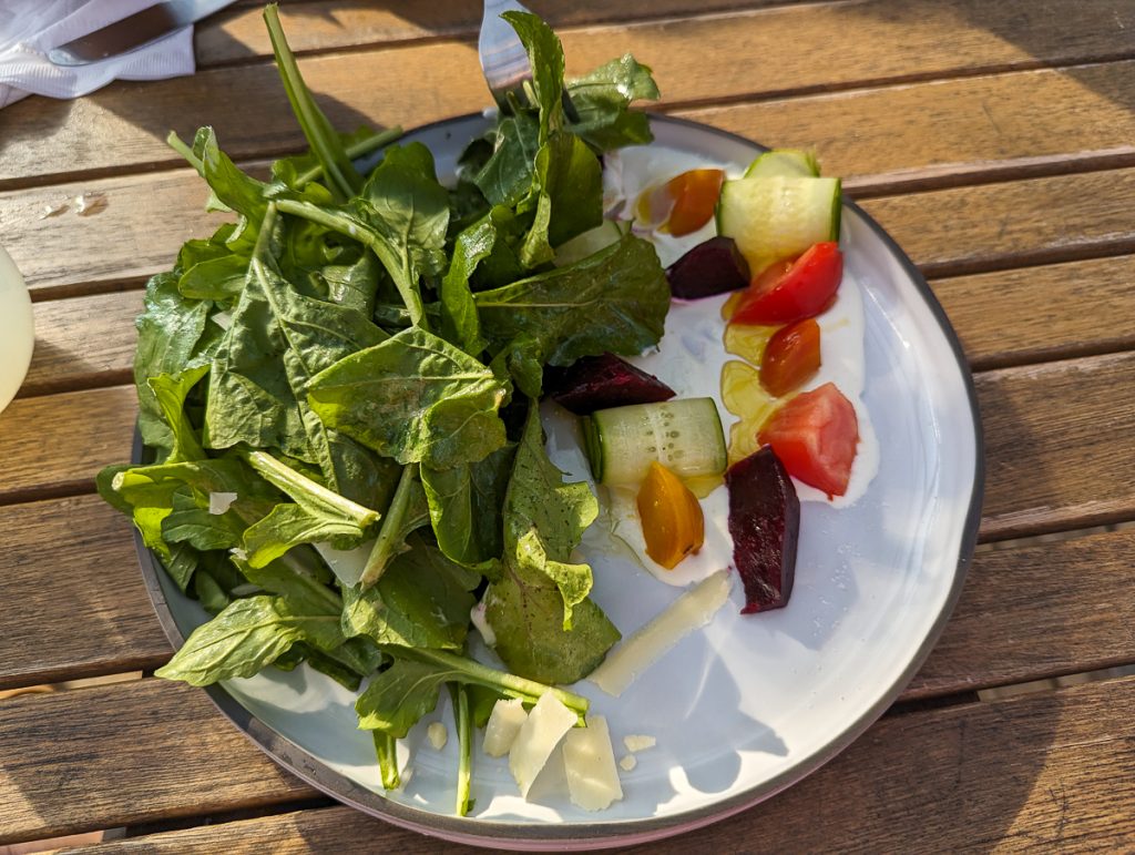 A close up shot of a white plate holding salad on a wooden surface.