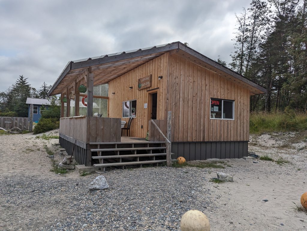 A wooden building with a balcony and steps leading from pebbly/sandy ground on an overcast day.