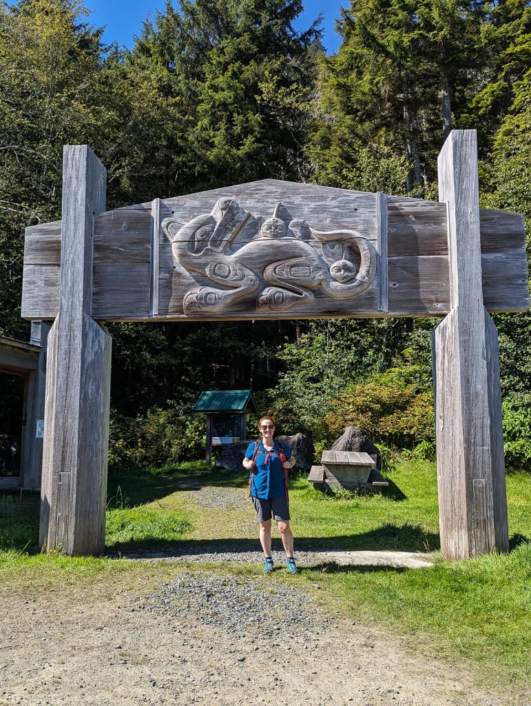 A woman stands under a gate carved by Bill Reid