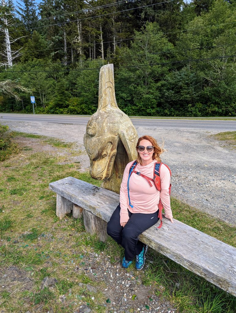 A woman sitting on a wooden bench next to a wooden carving of an orca.