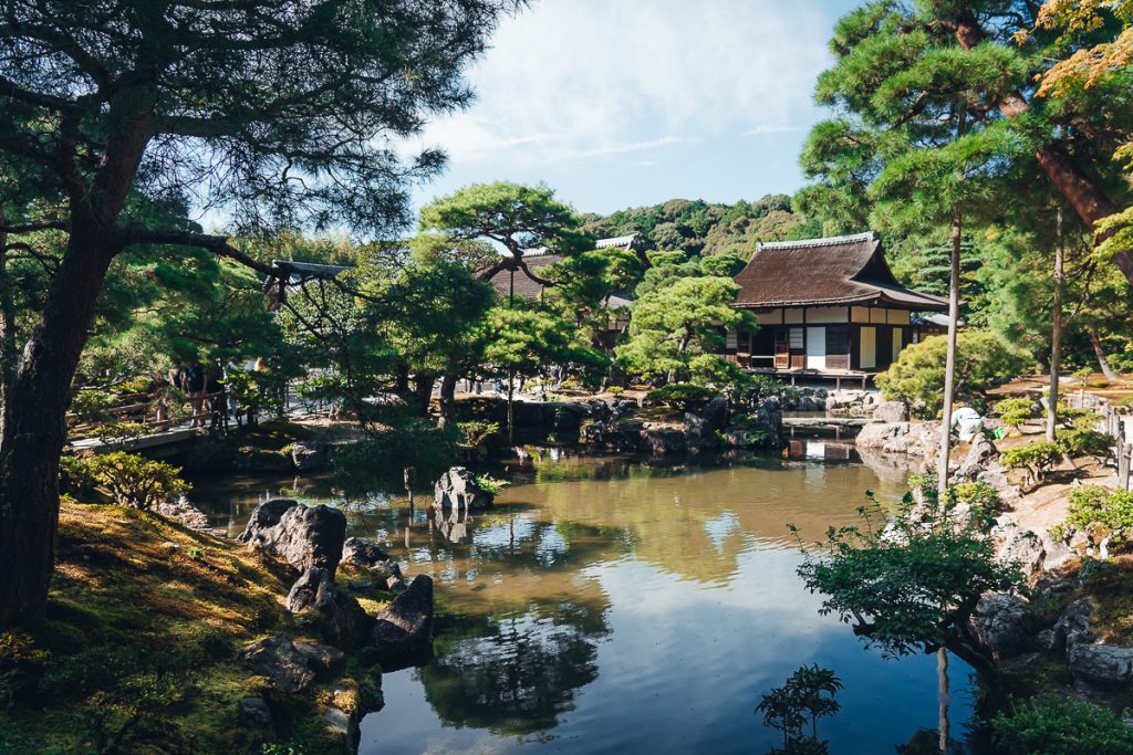 A pond surrounded by trees and a Japanese style building.