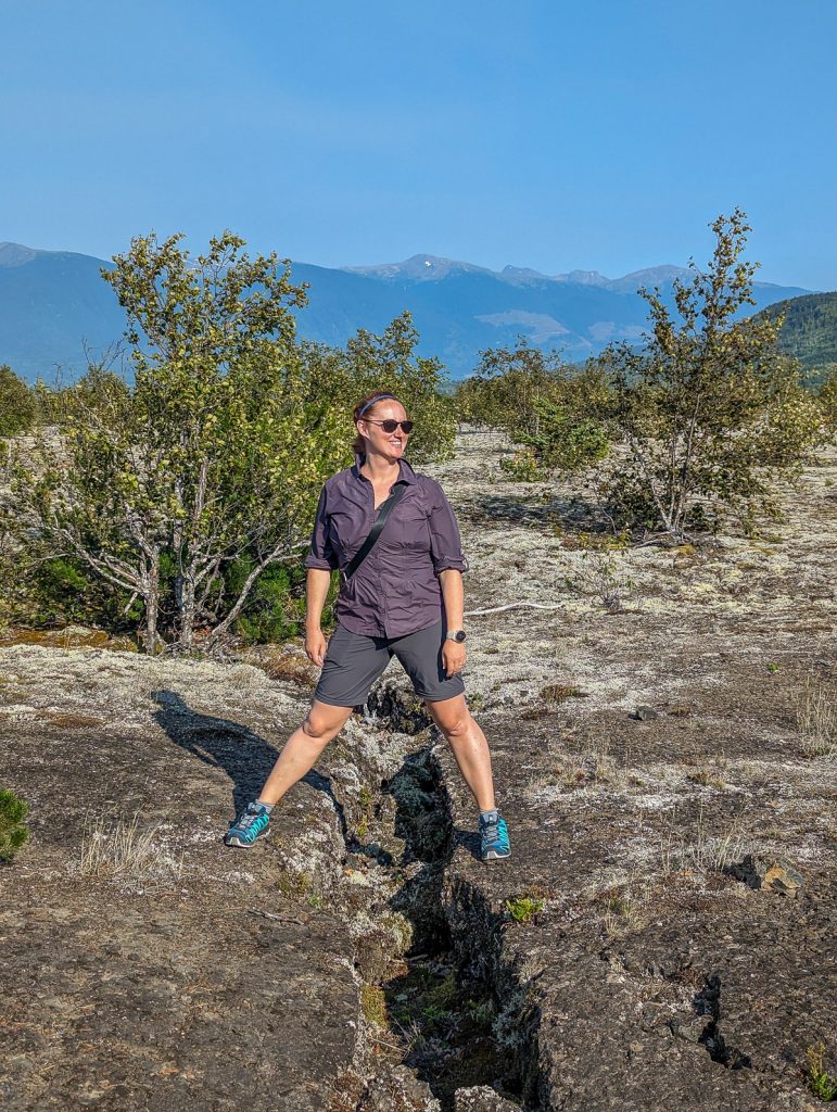 Sooz standing with each leg on either side of a crack in the lava rocks of the Nass Valley.