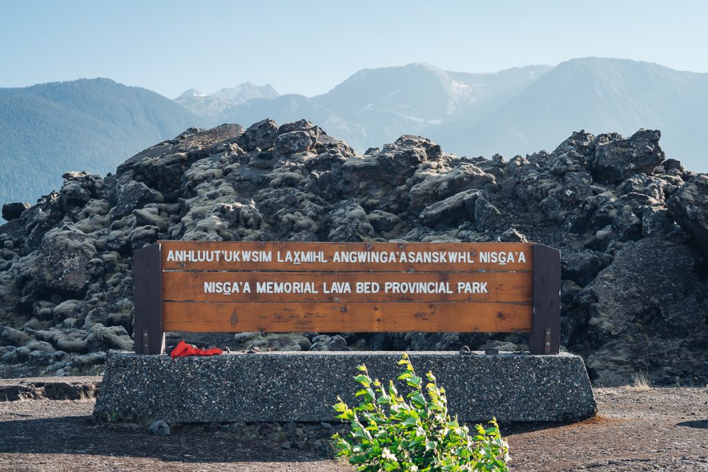 A sign indicating you are in the provincial park dedication site of the Nisga'a First Nation of Canada. Behind the sign is a lava bed.