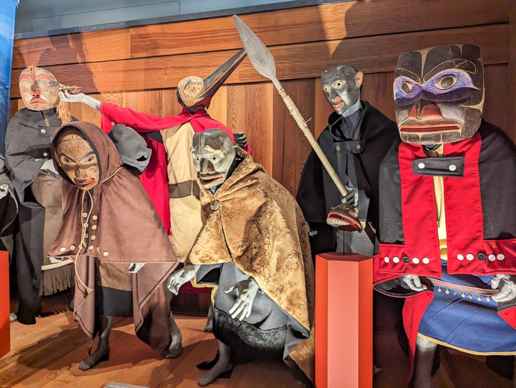 A museum exhibit showing figures wearing carved wooden masks and ceremonial clothing.