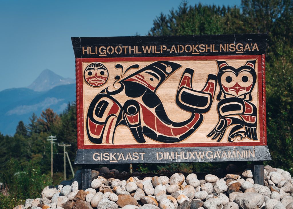 A beautiful carved sign for a Nisga'a Nation village with sylized orca and owl symbols painted in red and black.