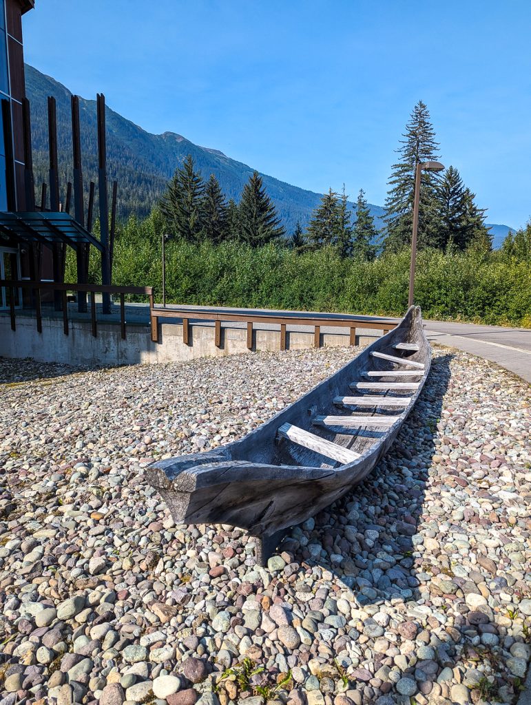 A traditional Nisga'a Nation canoe sitting on pebbled ground next to a road.