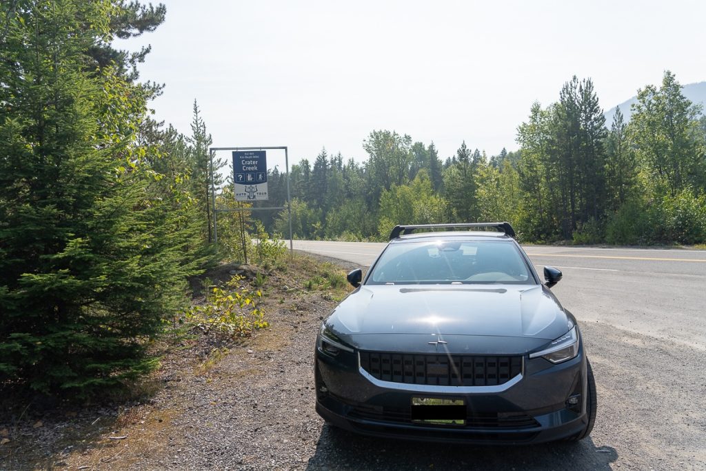 An electric car parked on the side of a road next to a Crater Creek Auto Tour sign.