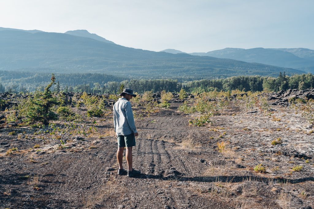 A man standing in a bare rocky area with wooded mountains in the background.