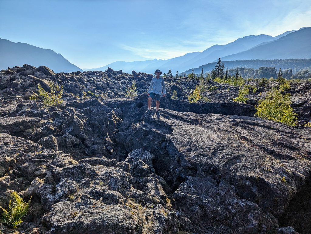 A man standing in an almost otherworldly rocky landscape with wooded mountains in the far background.