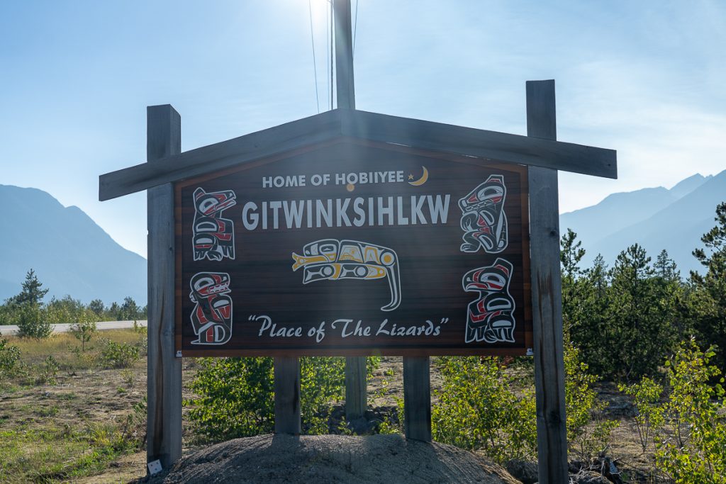 A wooden sign outside painted with symbolic animal symbols and text that reads "Home of Hobiiyee. Gitwinksihkkw. Place of the Lizards."