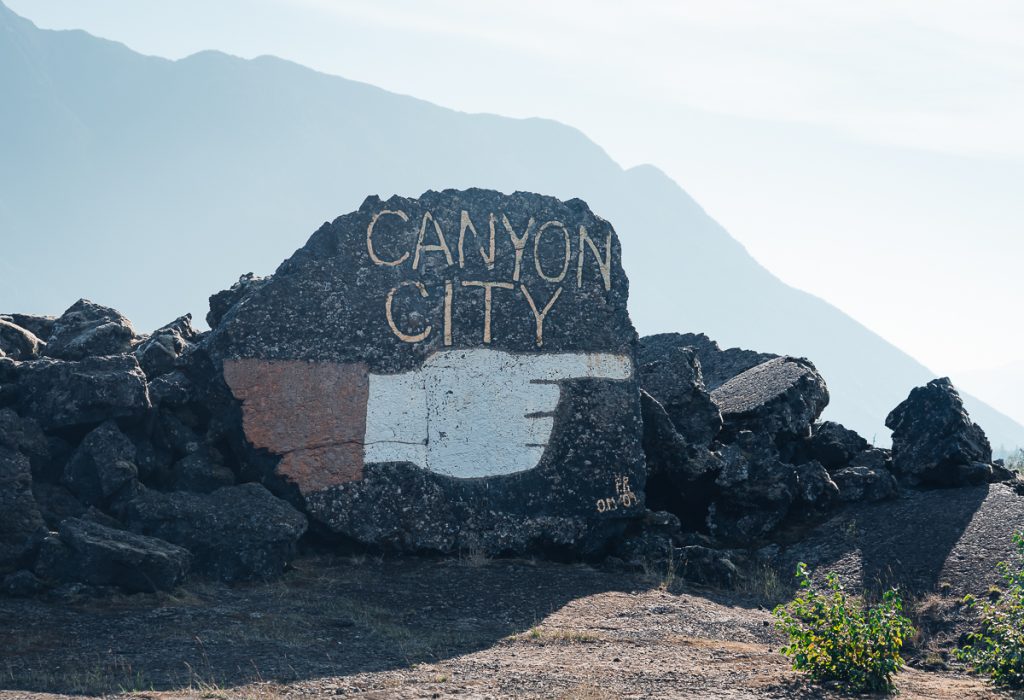 A large rock surrounded by smaller rocks, with a hand pointing and the words "Canyon City" painted on the large rock.