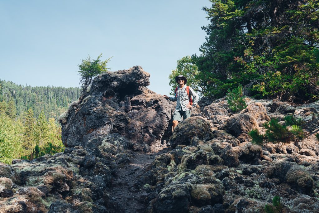A man in hiking gear surrounded by mossy rocks and smiling at the camera.