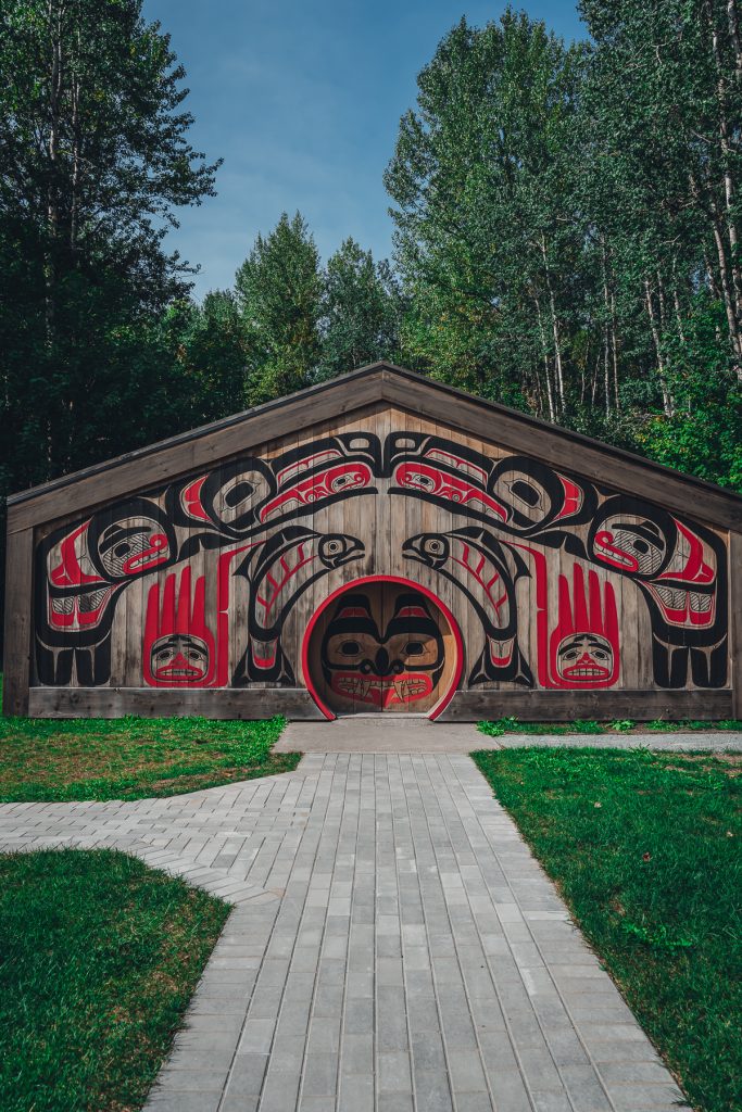 Front view of the Nisga'a National longhouse visitor center with the front door closed to properly show the red and black paintings of animals on the exterior.