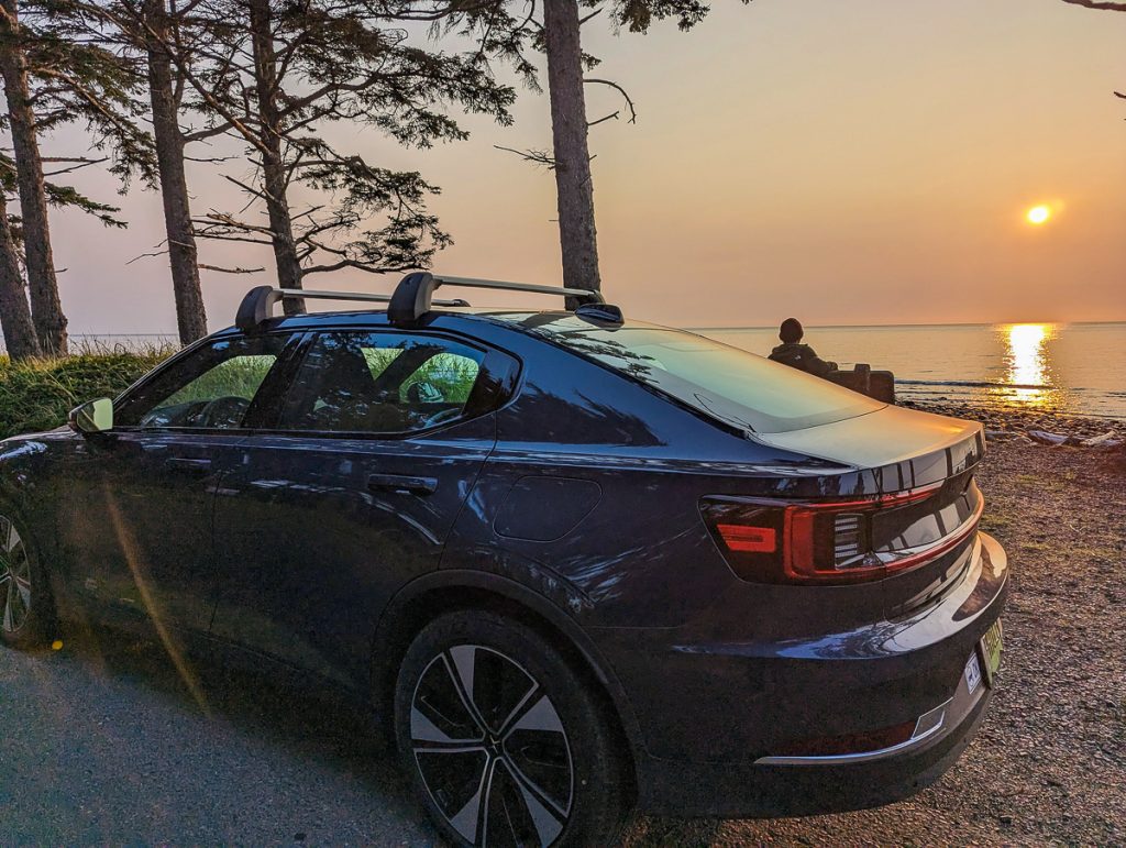 An electric vehicle parked next to water at sunset.