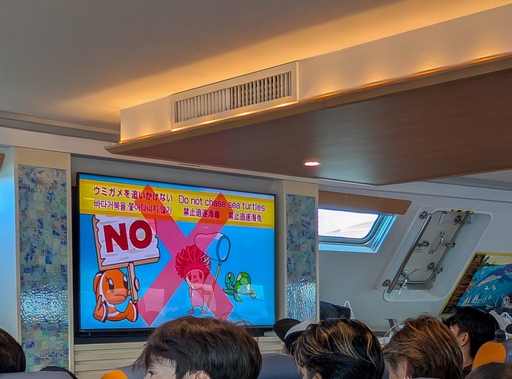 A sign on a boat telling tourists not to chase turtles while snorkelling, seen over the heads of people sitting on the boat.