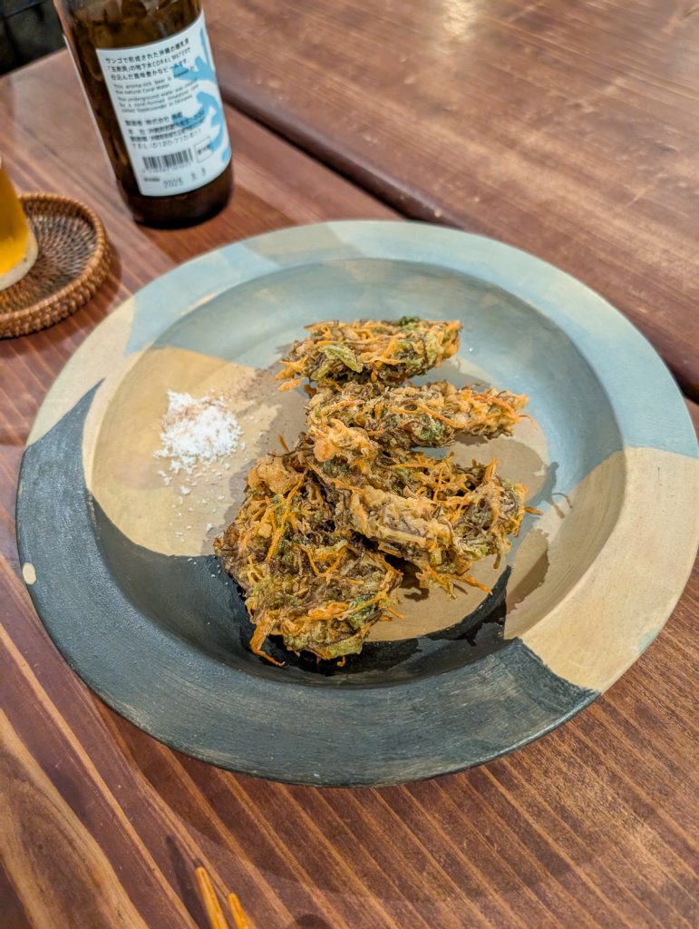 A black and brown plate on a wooden surface with green-ish brown food and some salt.